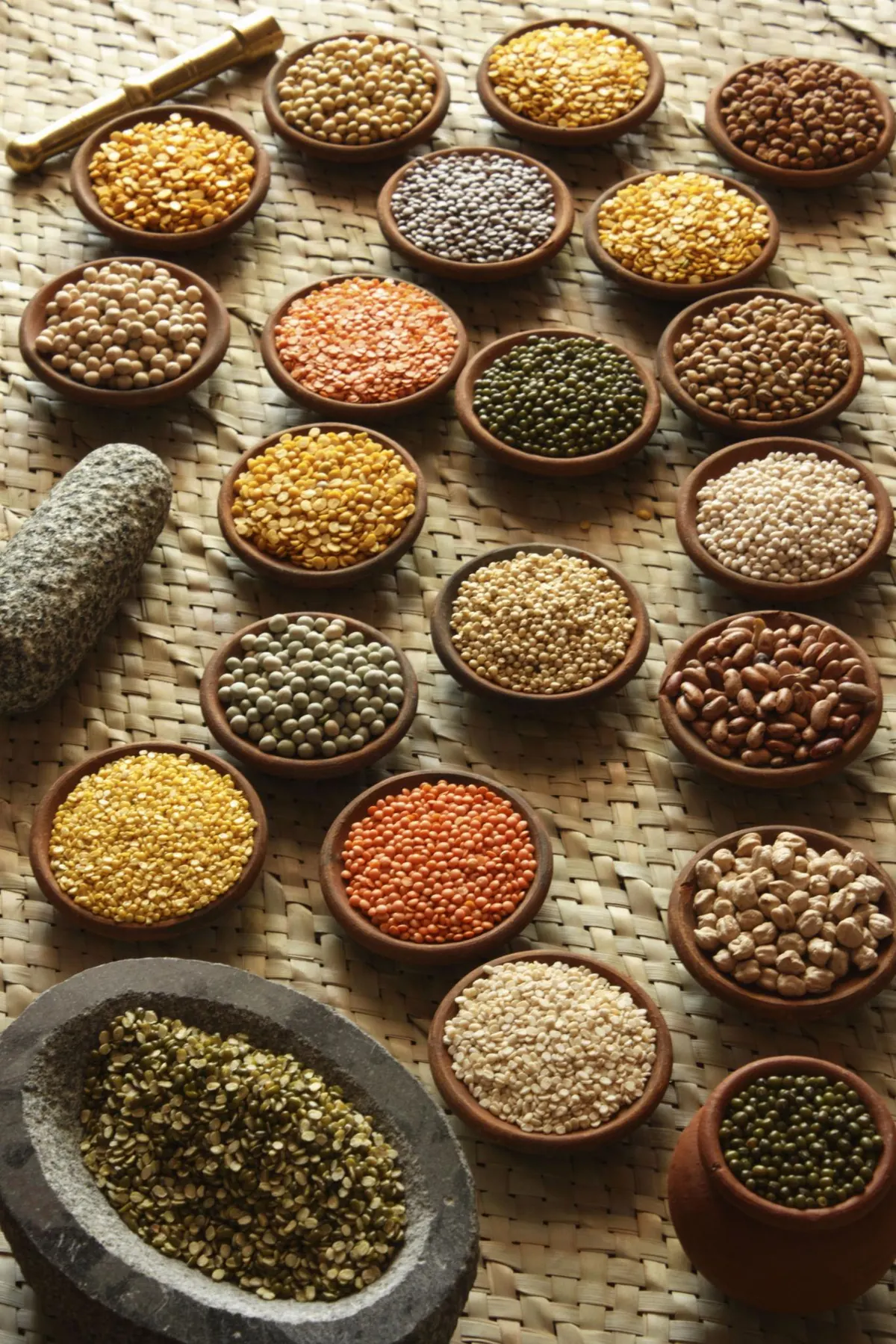 Clay bowls of lentils, gram and split pulses arranged on a woven mat.