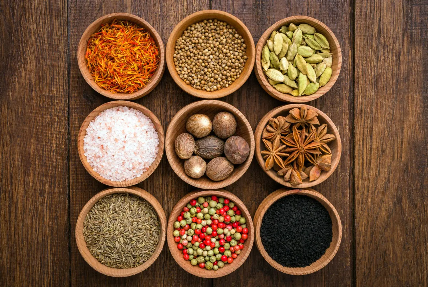 Whole spices arranged in wooden bowls, including cardamom, star anise and cumin.